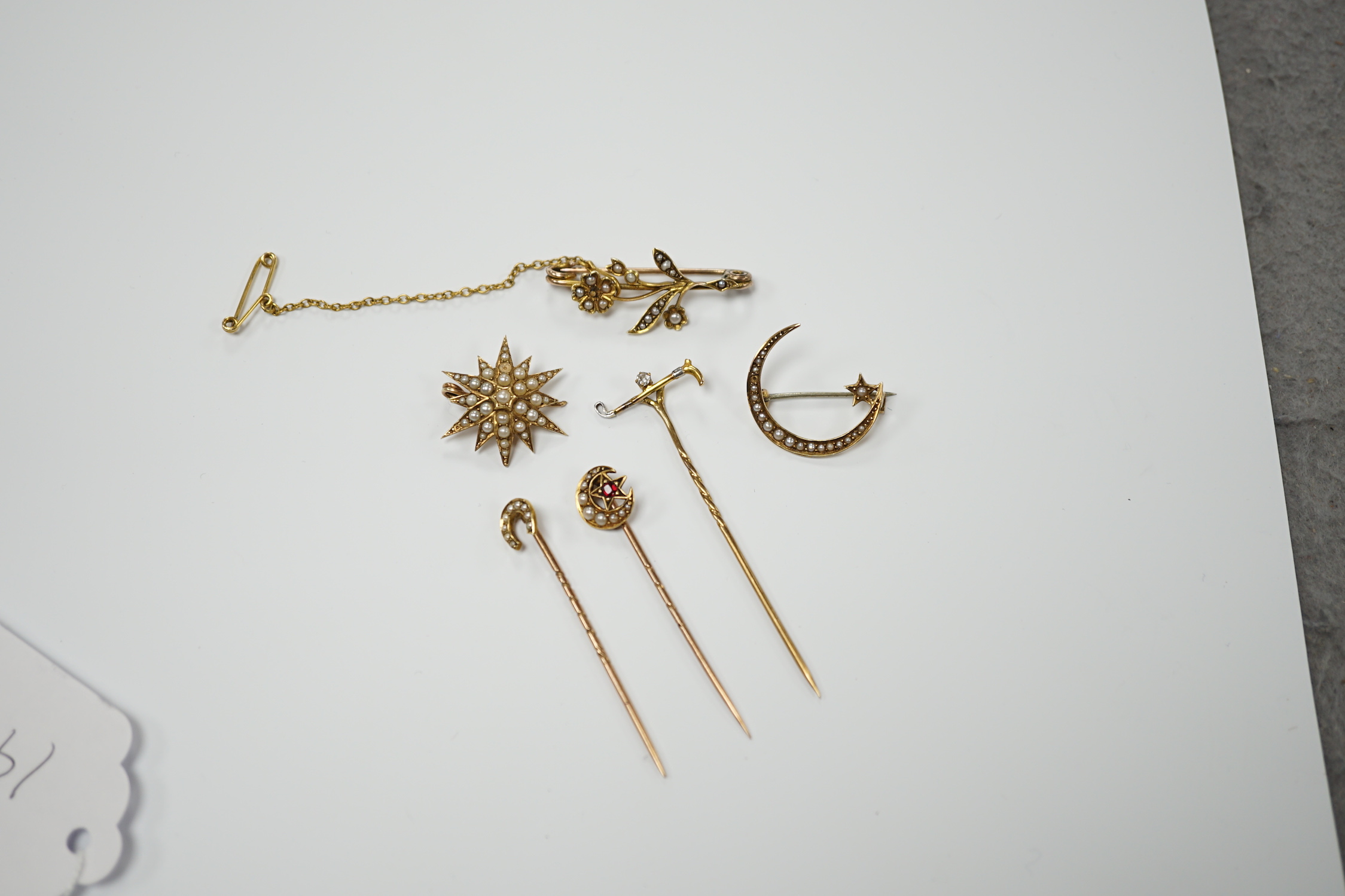 Three early to mid 20th century yellow metal and seed pearl set brooches, largest 34mm, two similar stick pins and a diamond set riding crop stick pin.